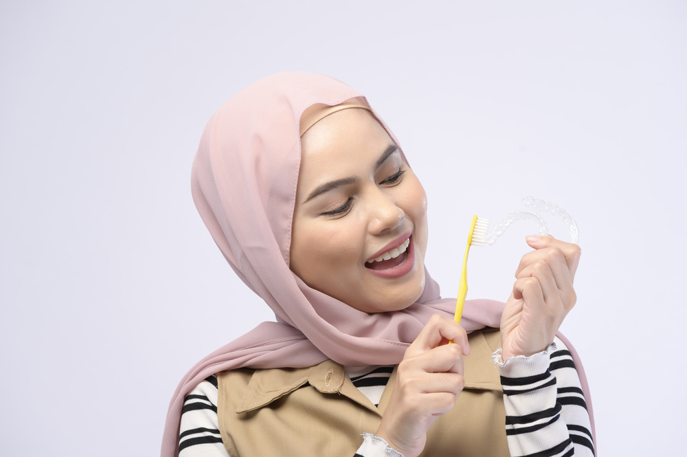 a young woman cleaning an Invisalign aligner with a toothbrush