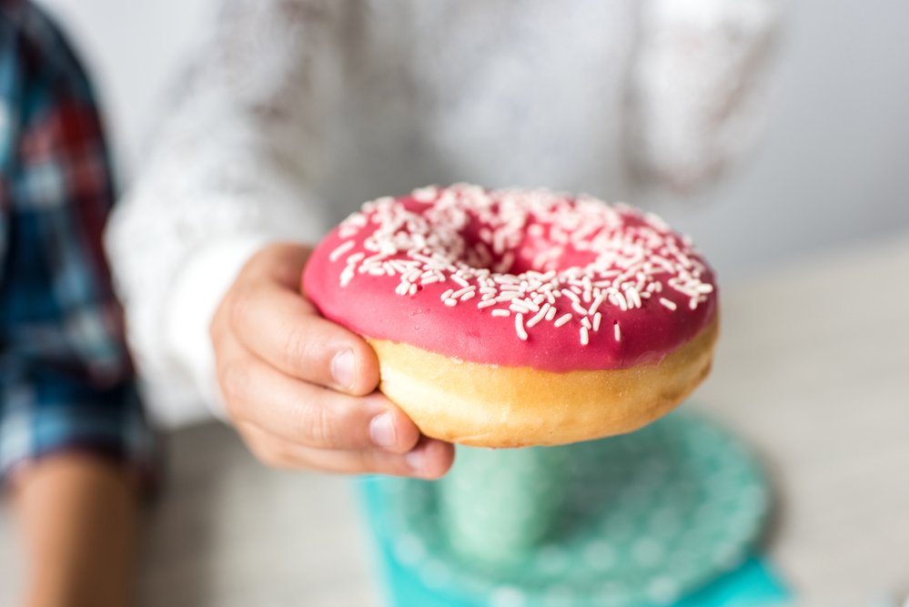 a person holding out a doughnut with pink frosting and white sprinkles