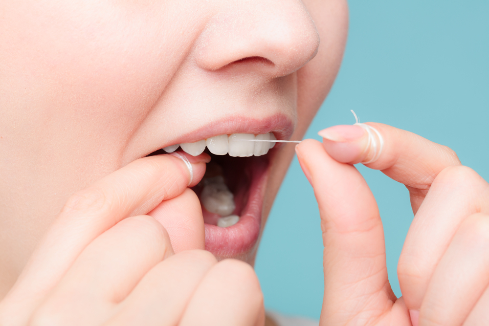 a young woman using dental floss to floss her teeth