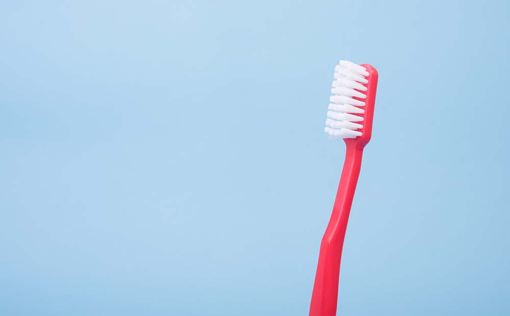A red toothbrush with white bristles against a blue background