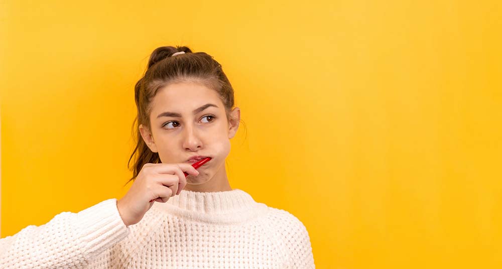A woman with a ponytail brushes her teeth against a bright yellow background