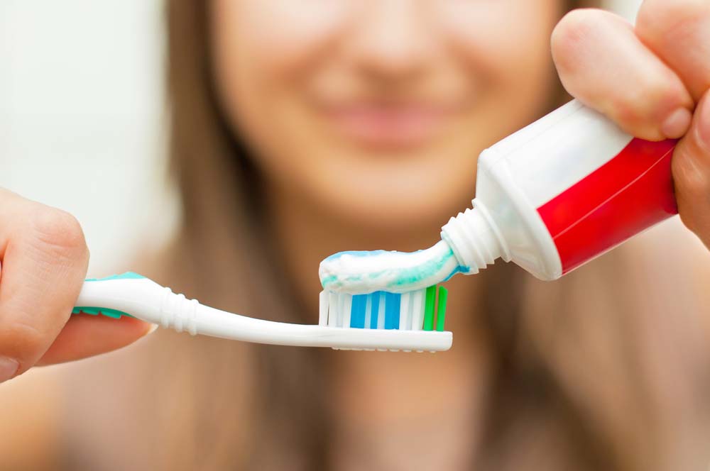 a smiling woman putting toothpaste on a toothbrush
