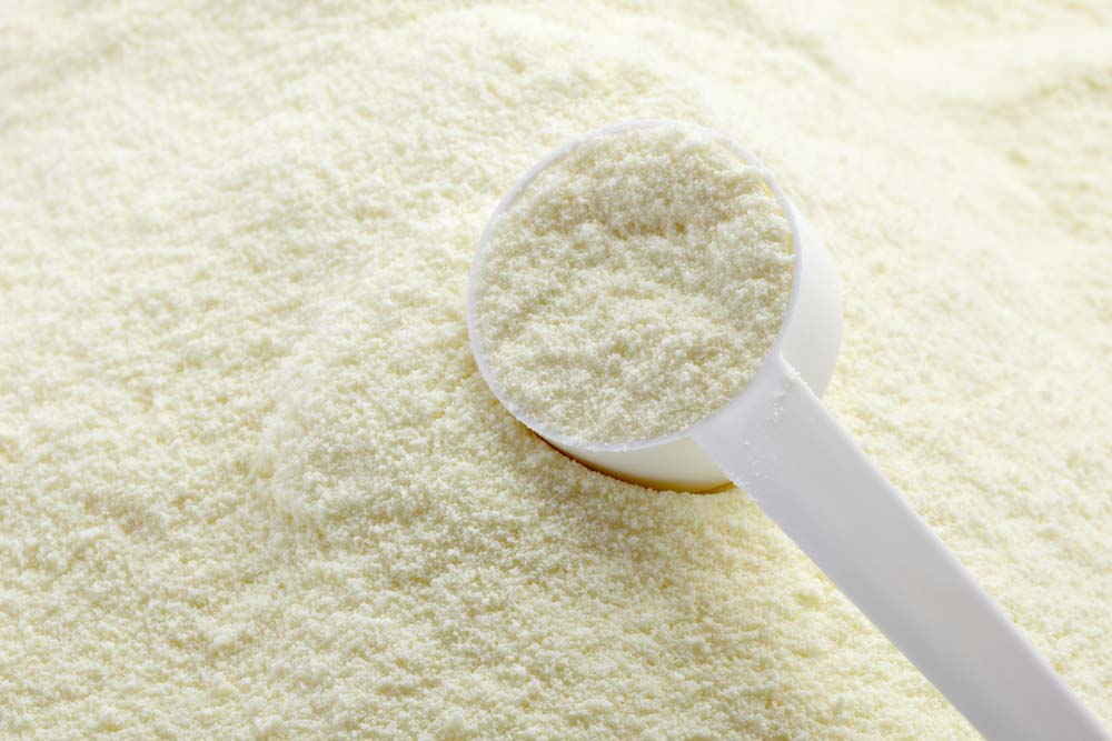 a measuring cup filled with powdered milk set on top of a pile of powdered milk on a countertop