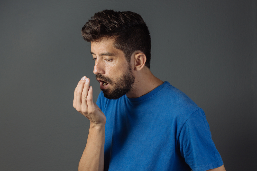 a young man with a beard breathing into his hand to check for bad breath