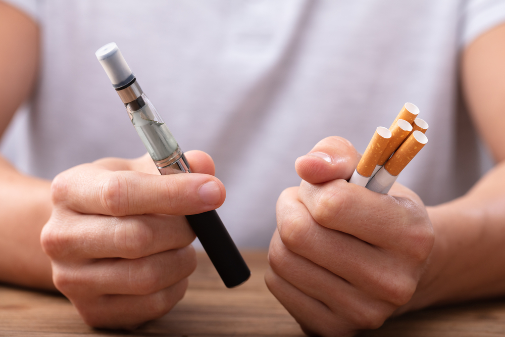 a man holding an e-cigarette in one hand and regular cigarettes in the other hand