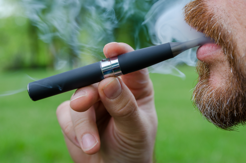 a man with a bead vaping with an e-cigarette outside in a backyard