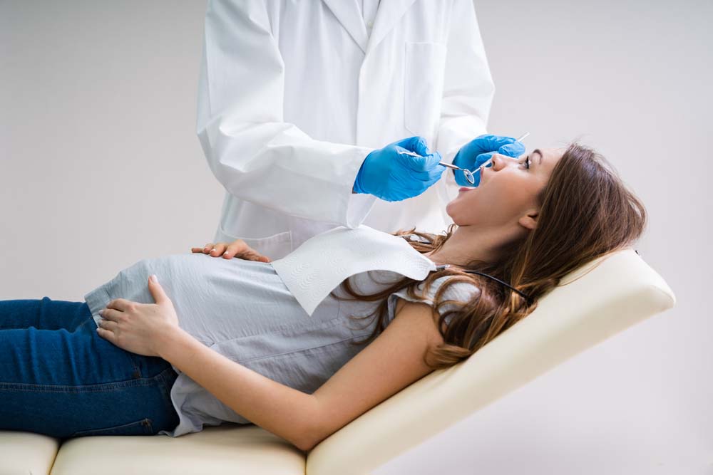 A dentist treats the teeth of a pregnant woman, who is reclined in a dentist’s chair.
