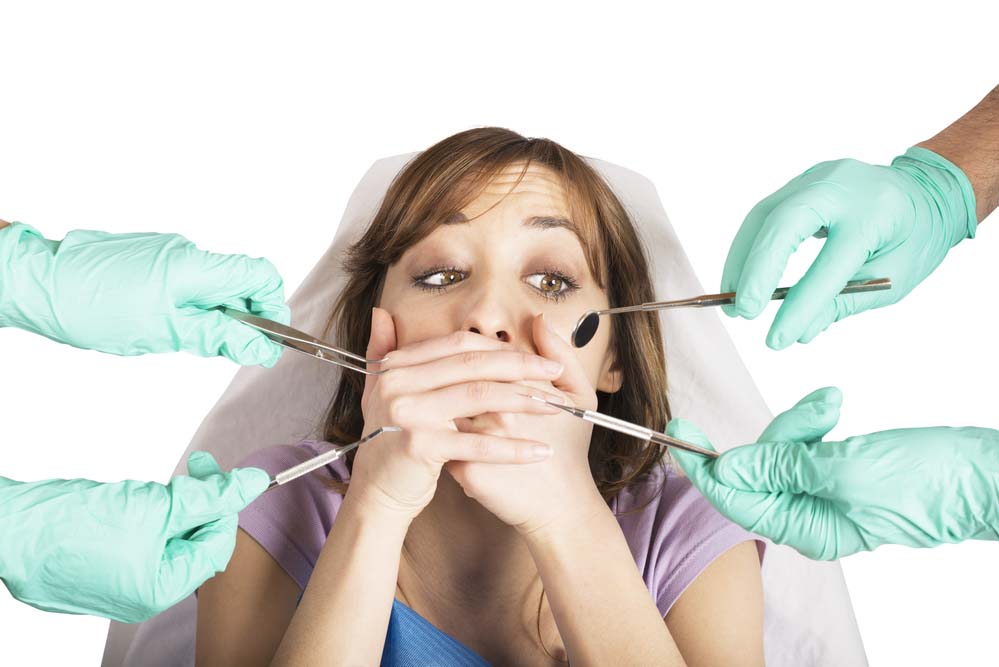A woman looks scared and puts her hands over her mouth as her hands try to put dental tools in it.