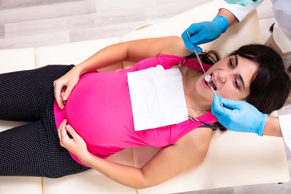 An overhead shot of a pregnant woman getting treated by a dentist.