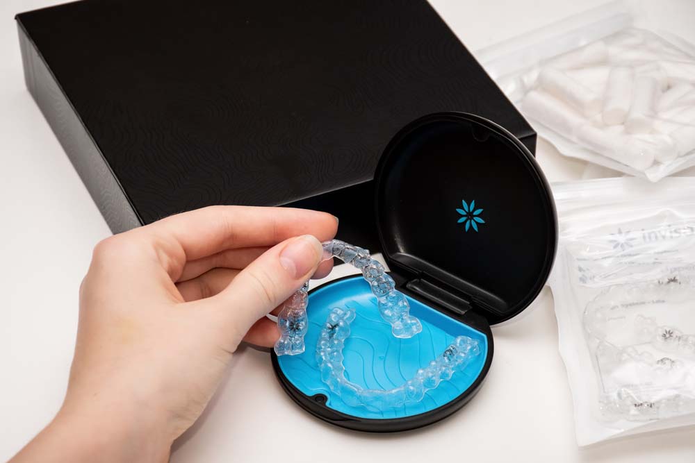 A person holding one side of Invisalign aligners and the other side of the aligners are still in the packaged container.