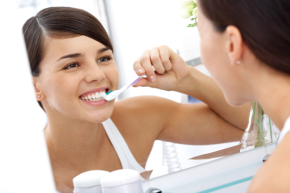 a young woman brushing her teeth in a mirror
