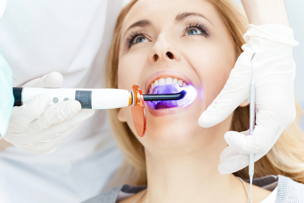 Close-up partial view of a dentist using dental curing UV lamp on teeth of the patient