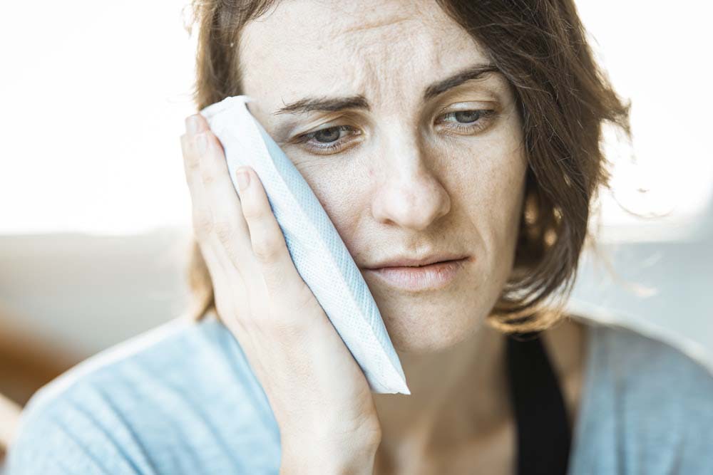 Woman holding a pack of ice to her face while looking in pain.